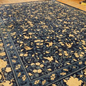 Navy rug with a dense all-over pattern of yellow birds and flowers, displayed on wood plank flooring.