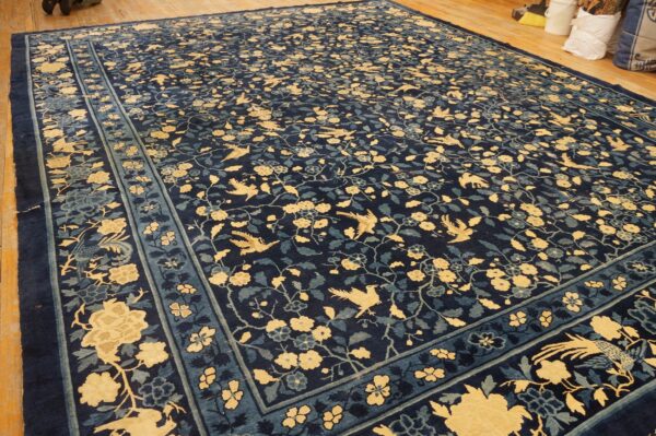 Navy rug with a dense all-over pattern of yellow birds and flowers, displayed on wood plank flooring.