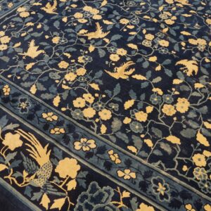 A dark blue rug featuring a golden yellow and teal pattern of flowering vines and stylized birds.