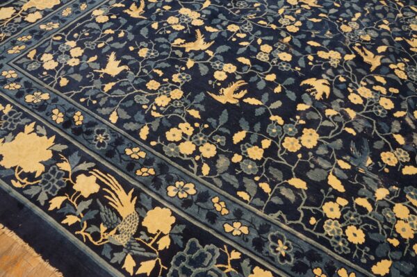 A dark blue rug featuring a golden yellow and teal pattern of flowering vines and stylized birds.