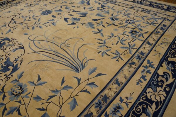 Large tan rug with dark blue and light blue stylized floral vines and wide, layered borders.