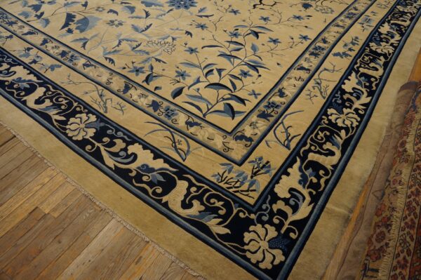 Beige rug featuring a detailed blue floral pattern and multi-layered border on wooden planks.