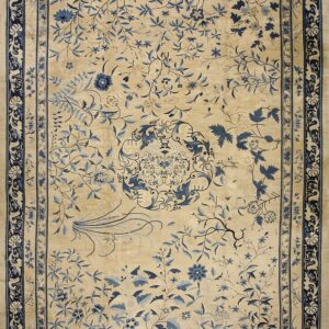 A large beige rug featuring an intricate blue floral vine pattern and a wide navy border.