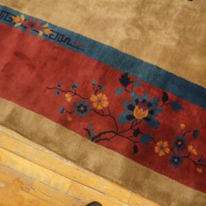 Detail of a plush tan rug with a diagonal red band featuring blue and gold floral designs on wood flooring.