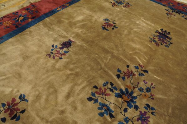 A lustrous tan rug features sparse blue, red, and purple floral motifs bordering a wide patterned red band.