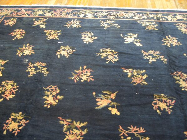 Dark blue rug with scattered pink and gold floral sprigs and a matching border on wood floors.