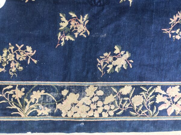 Navy blue rug detail featuring pink and ivory floral patterns and a wide ornamental border band.