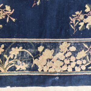 Close-up of a dark blue rug with a wide floral border in pale yellow, muted pink, and olive green.