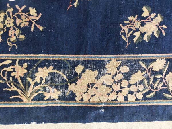 Close-up of a dark blue rug with a wide floral border in pale yellow, muted pink, and olive green.