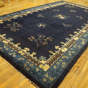 Large navy blue rug with tan and light blue floral and geometric borders sits on golden plank flooring.