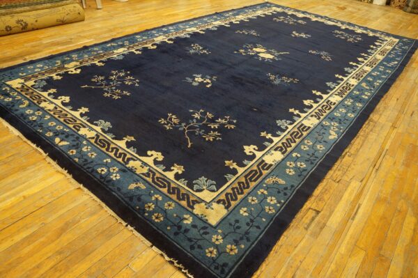 Large navy blue rug with tan and light blue floral and geometric borders sits on golden plank flooring.