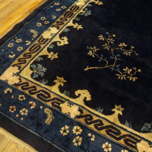 High-pile navy rug featuring gold floral branches and detailed geometric borders on a light wood floor.