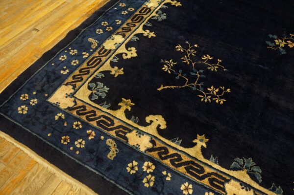 High-pile navy rug featuring gold floral branches and detailed geometric borders on a light wood floor.
