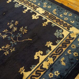 A dark blue rug with gold flowering vines and detailed blue and tan borders rests on wood plank flooring.