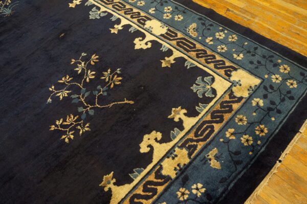 A dark blue rug with gold flowering vines and detailed blue and tan borders rests on wood plank flooring.