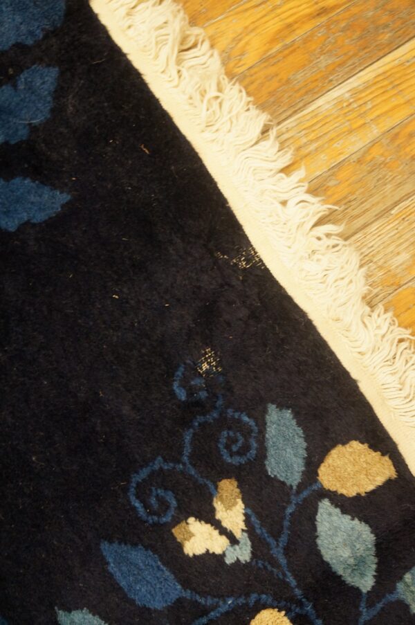 High-pile navy rug with blue and tan floral patterns and cream fringe rests on a wood floor.