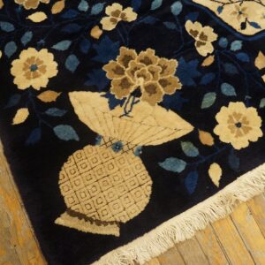 High-pile navy rug corner showing beige flowers and an intricate vase motif on yellow plank flooring.
