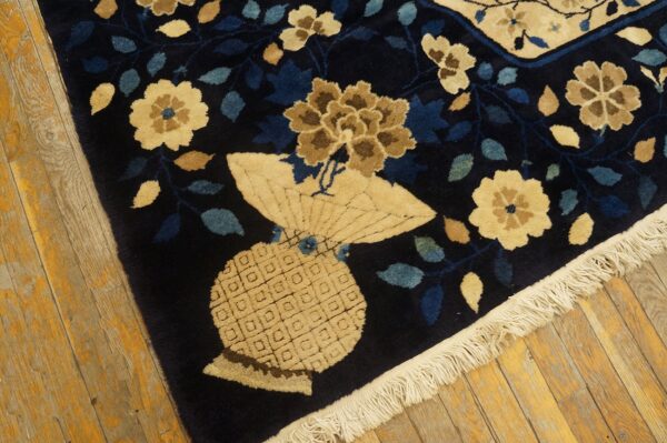 High-pile navy rug corner showing beige flowers and an intricate vase motif on yellow plank flooring.