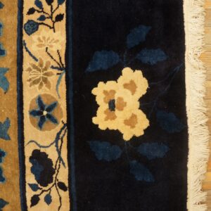 Navy and tan floral rug featuring a dense pile and white fringe, lying on light distressed wood planks.