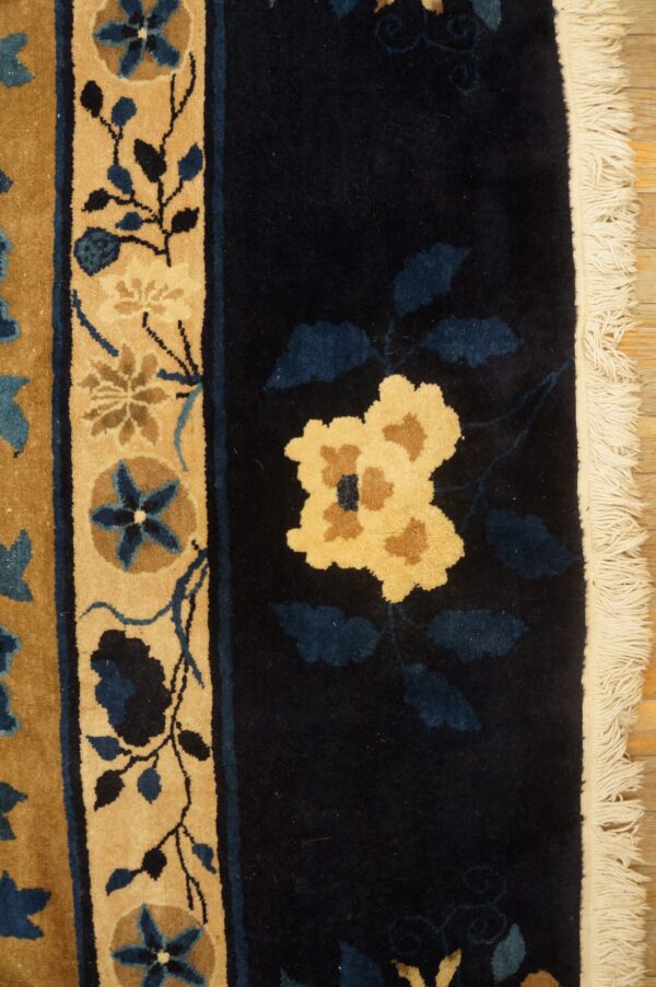 Navy and tan floral rug featuring a dense pile and white fringe, lying on light distressed wood planks.