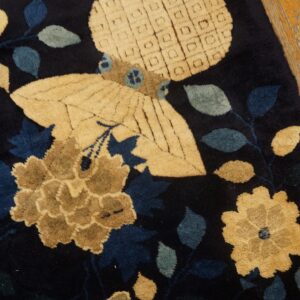 High-pile navy rug displays tan flowers, blue leaves, and a butterfly motif against distressed wood flooring.