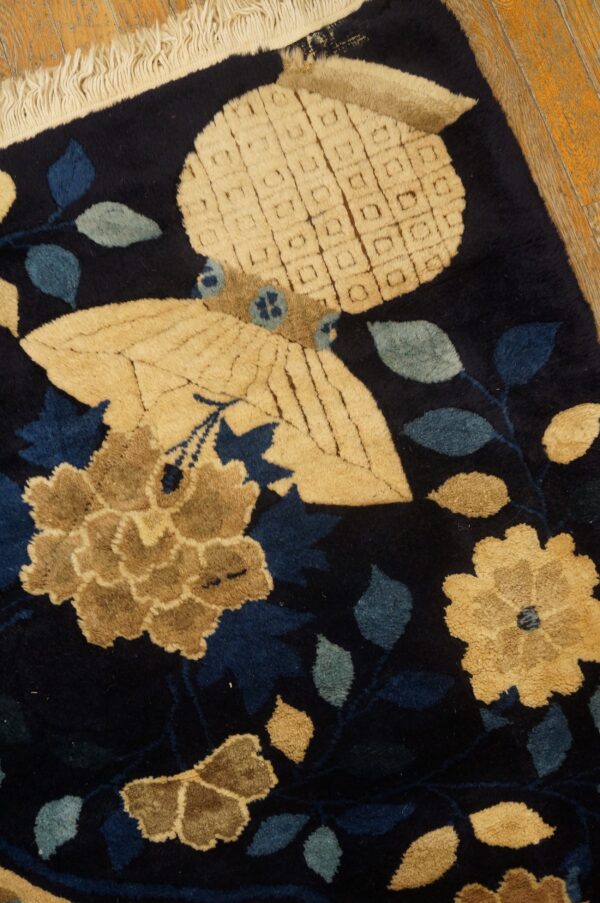 High-pile navy rug displays tan flowers, blue leaves, and a butterfly motif against distressed wood flooring.