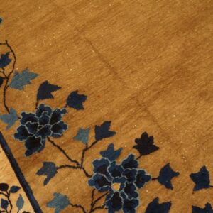 Close-up of a camel rug with a deep navy and light blue floral vine pattern border.