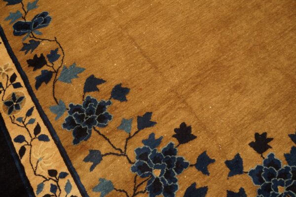 Close-up of a camel rug with a deep navy and light blue floral vine pattern border.