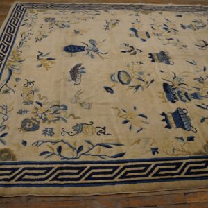 Cream rug with blue and gold scattered designs and geometric border rests on dark wood planks.
