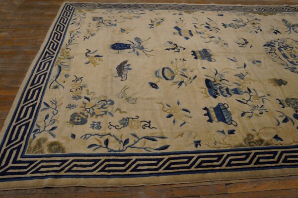 Cream rug with blue and gold scattered designs and geometric border rests on dark wood planks.