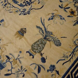 Beige rug with intricate blue and gold chinoiserie patterns and a dark blue geometric key border.