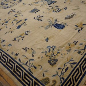 Low-pile beige rug with scattered blue botanical and vase motifs, bordered by a navy Greek key pattern.