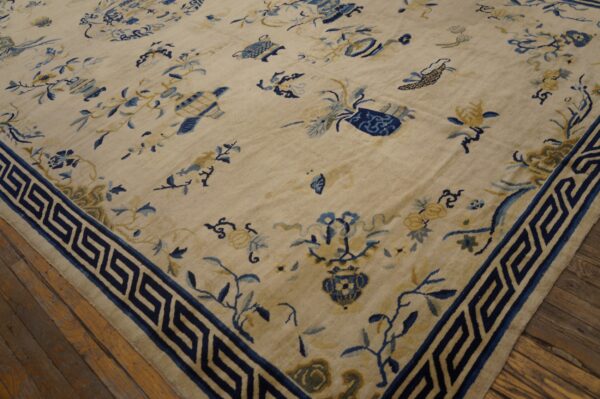 Low-pile beige rug with scattered blue botanical and vase motifs, bordered by a navy greek key pattern.