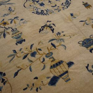 Low-pile beige rug patterned with light blue and gold florals, vases, and a dark geometric border.