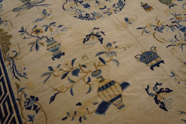 Low-pile beige rug patterned with light blue and gold florals, vases, and a dark geometric border.