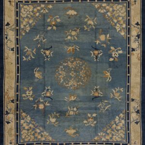Muted blue rug with light tan scattered floral and medallion patterns, framed by navy blue and beige borders.