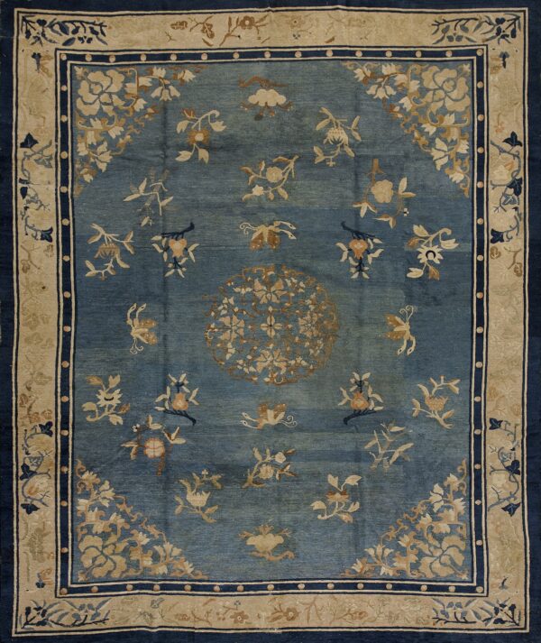 Muted blue rug with light tan scattered floral and medallion patterns, framed by navy blue and beige borders.