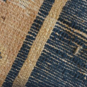 Close-up showing a textured low pile rug in tan, navy, and light blue with an exposed striped woven edge.