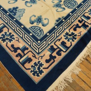 Navy, pink, and ivory rug corner with detailed geometric and floral borders resting on aged wood floorboards.