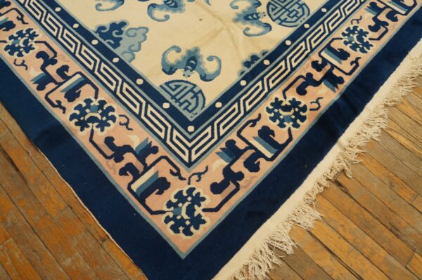 Navy, pink, and ivory rug corner with detailed geometric and floral borders resting on aged wood floorboards.
