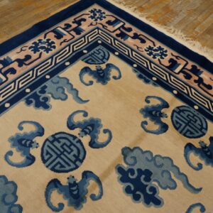 Tan rug with blue cloud and bat motifs, contrasting navy and pink geometric borders, on wood planks.