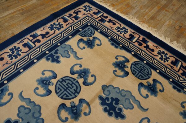 Tan rug with blue cloud and bat motifs, contrasting navy and pink geometric borders, on wood planks.