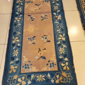 Tan field runner rug with blue borders featuring yellow and light blue floral vine designs on tiled flooring.