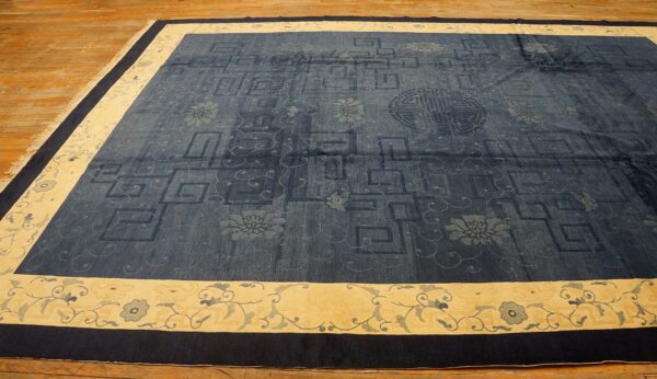 Dark blue patterned rug with tone-on-tone fretwork and florals, framed by a wide cream and dark navy border.