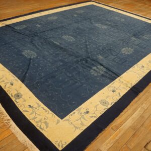 Low-pile indigo rug featuring scrolling floral motifs and a wide, creamy yellow floral border on a wood floor.