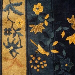 Close-up of a high-pile rug with navy, gold, and blue floral motifs bordering light wood flooring.