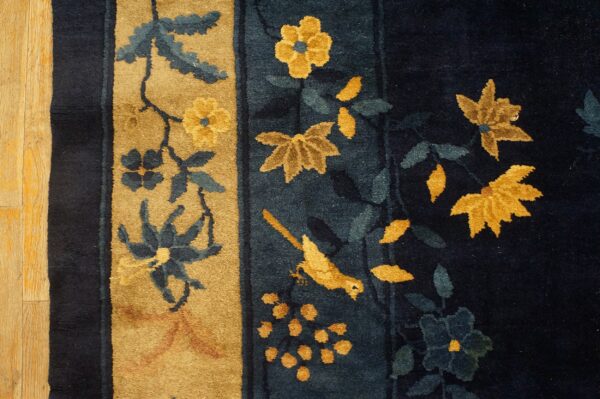 Close-up of a high-pile rug with navy, gold, and blue floral motifs bordering light wood flooring.