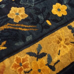 A high-pile rug features dark blue and gold floral patterns with a thick contrasting gold border.