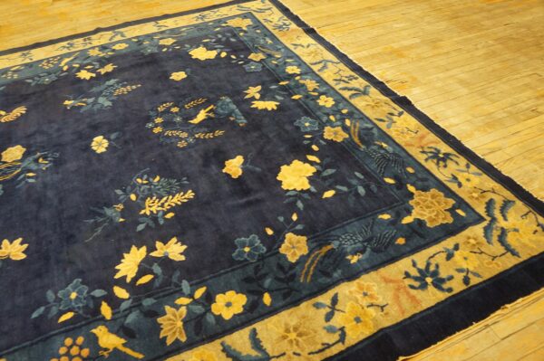 Navy rug with intricate yellow floral and bird patterns features a golden border on wood flooring.