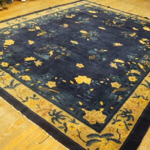 Square navy blue rug with gold and teal floral and bird patterns on light wood floors.